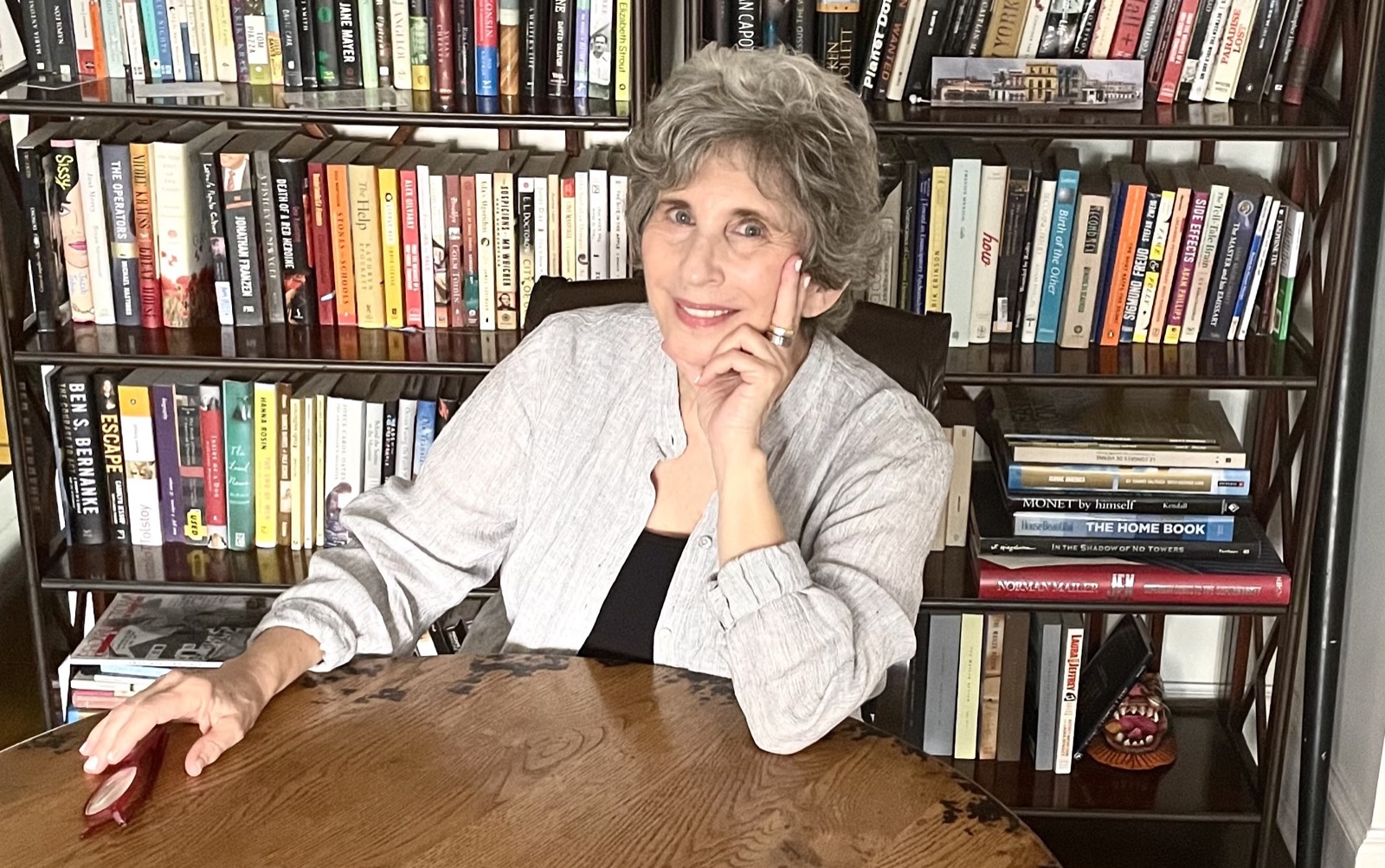 Susan Mailer seated in front of crowded bookshelves, chin resting on her hand